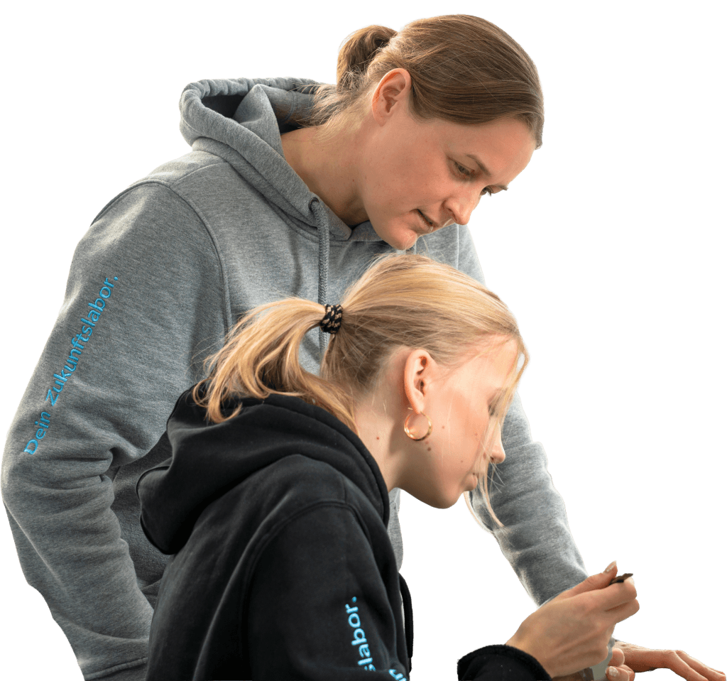 Zwei Frauen in Hoodies, eine ältere und eine jüngere, schauen gemeinsam auf ein kleines Objekt, das die jüngere Frau in den Händen hält.